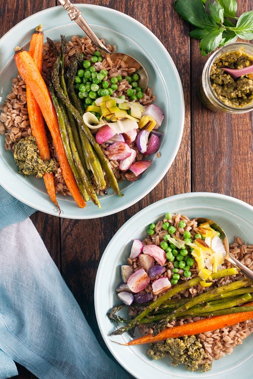 Two farro grain bowls topped with carrots, asparagus, peas, and pesto. 