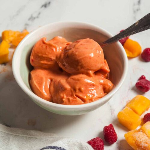 A big bowl of raspberry sorbet on a white marble background.