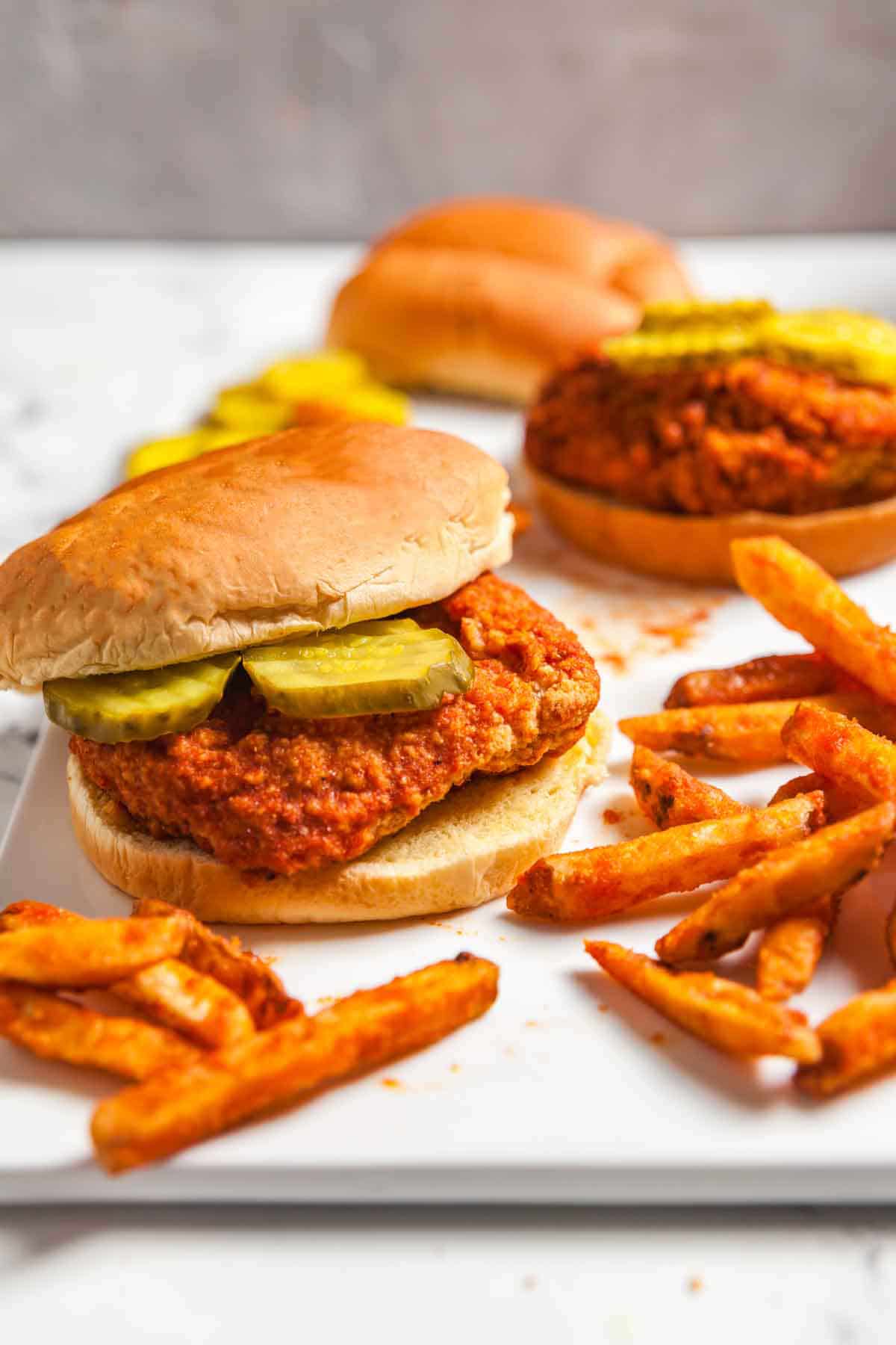 Two air fried Nashville hot chicken sandwiches with pickles surrounded by fries.