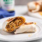 green chile chorizo breakfast burrito on a white plate with salsa in the background.