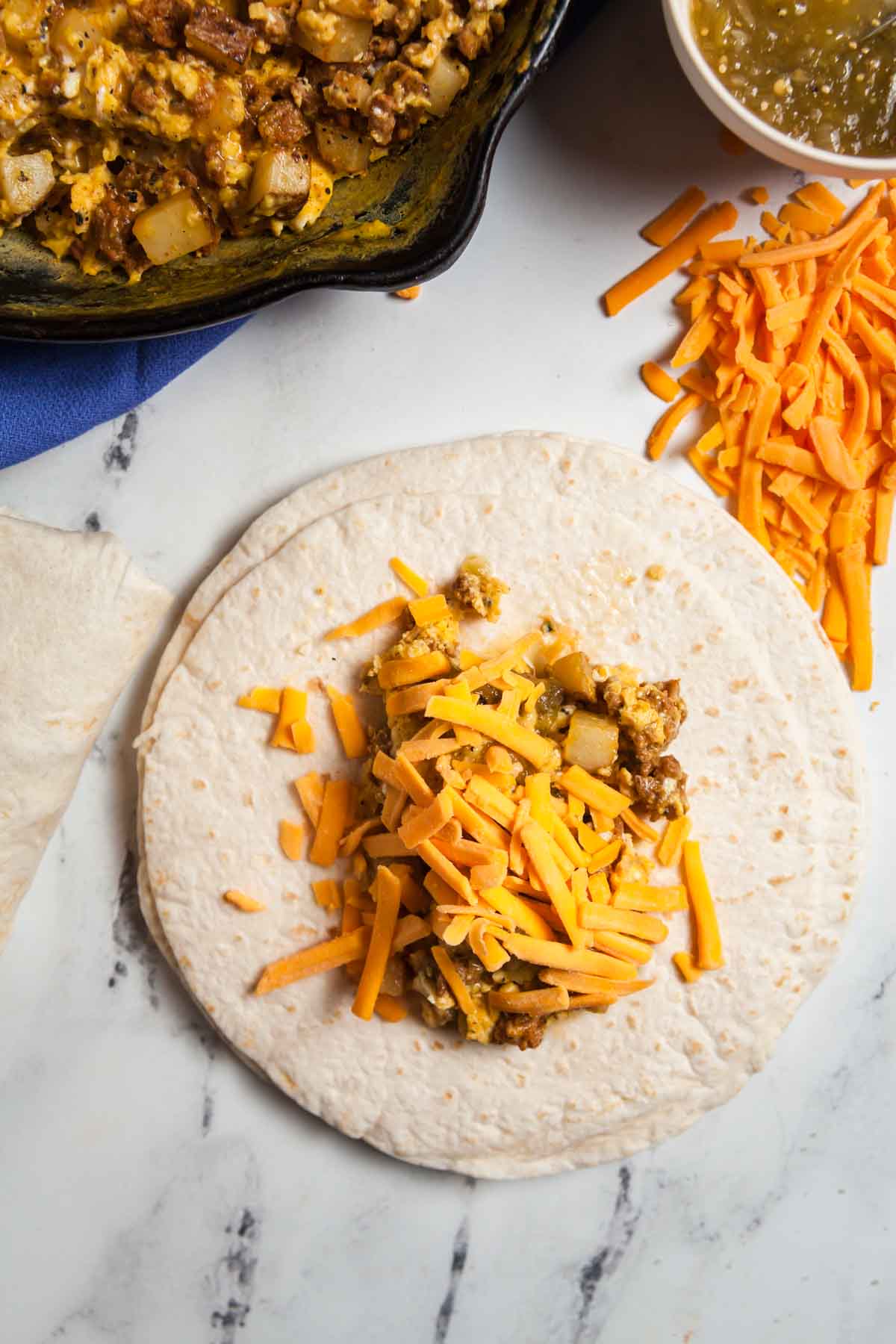 Placing the fillings on the tortilla to make freezer-friendly, meal-prep breakfast burritos.
