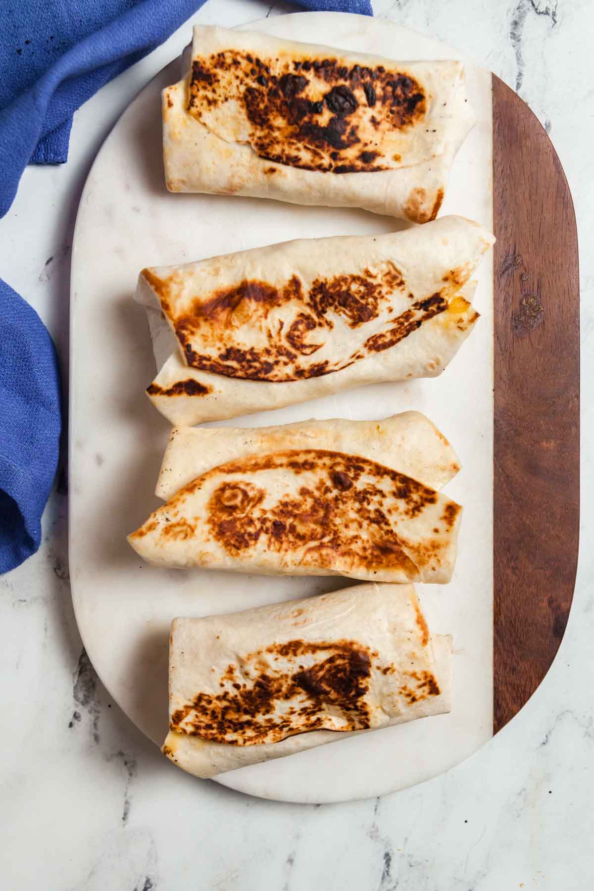 four breakfast burritos on a marble board.