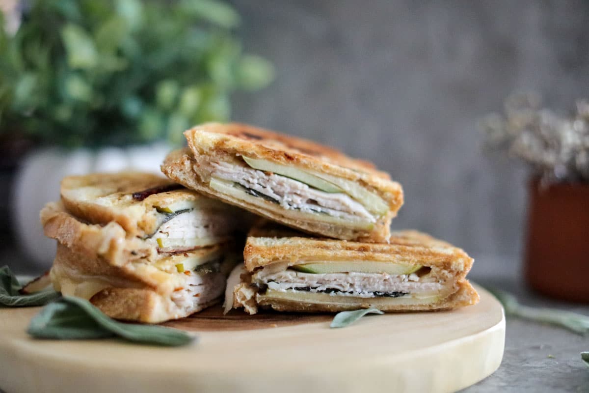 A pile of turkey panini sandwiches on a wooden board.