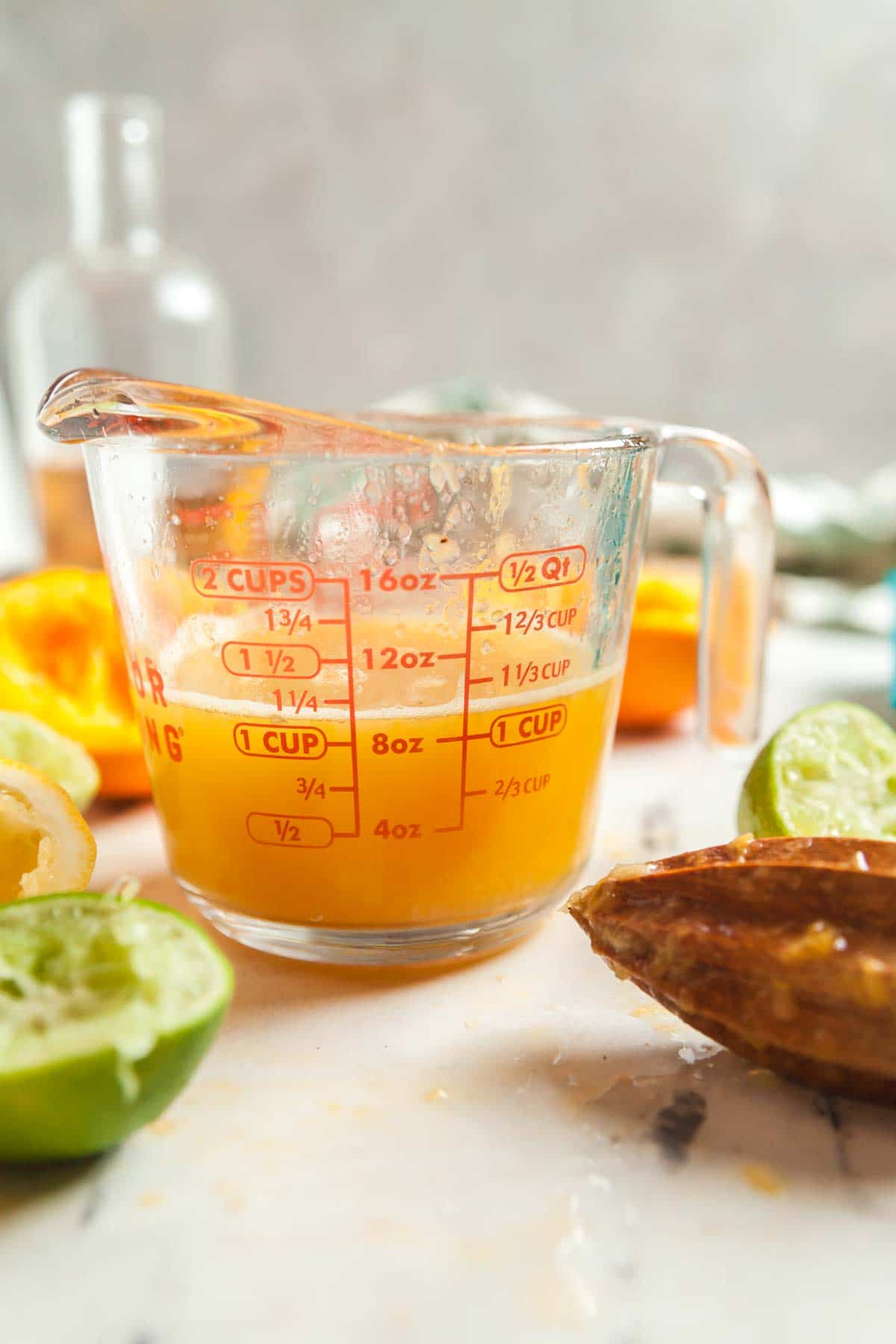 A measuring cup filled with citrus juice, surrounded by citrus peels and a reamer.