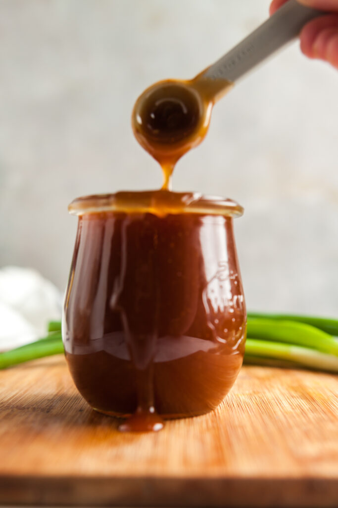 A small glass container of homemade teriyaki sauce with a spoon to show the gloss and thick consistency.
