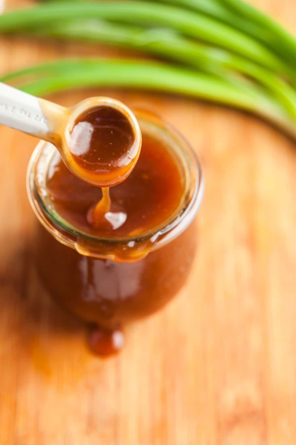3/4 view of teriyaki sauce dripping off a spoon to show its thick, glossy texture.