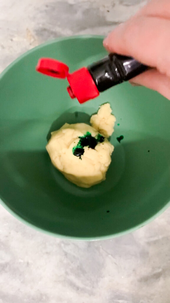 Mixing green food coloring into sugar cookie dough.