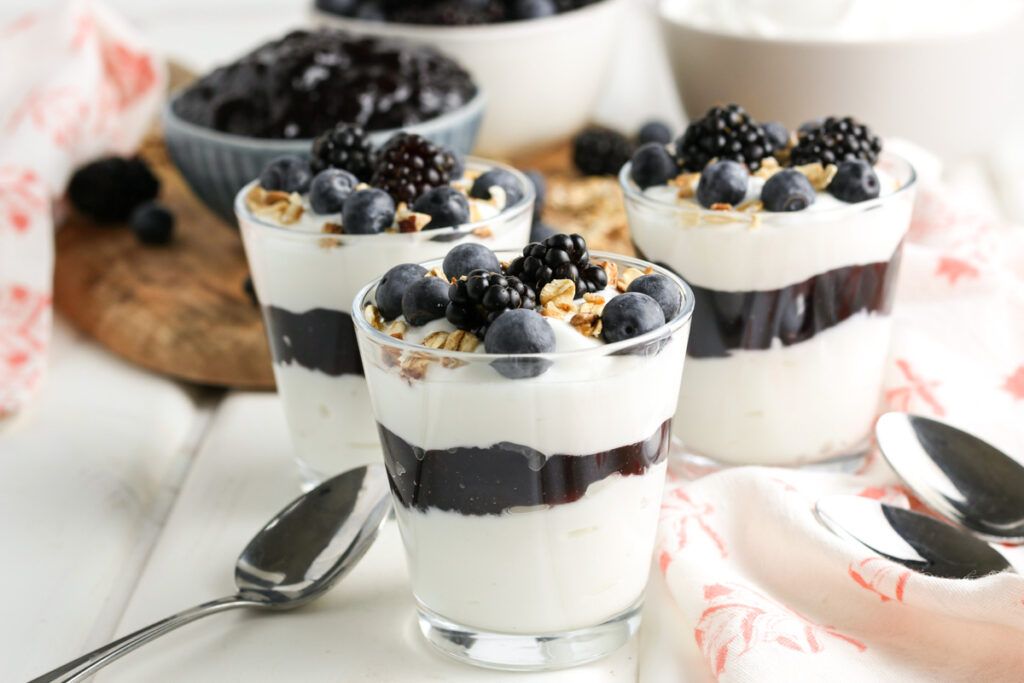 Landscape image of three blackberry and Greek yogurt parfaits topped with granola and fresh berries. 