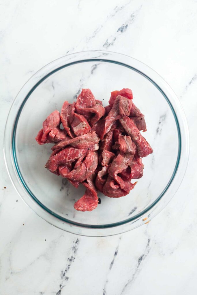 Overhead view of a bowl of thinly sliced sirloin steak for cheesesteak sandwiches.