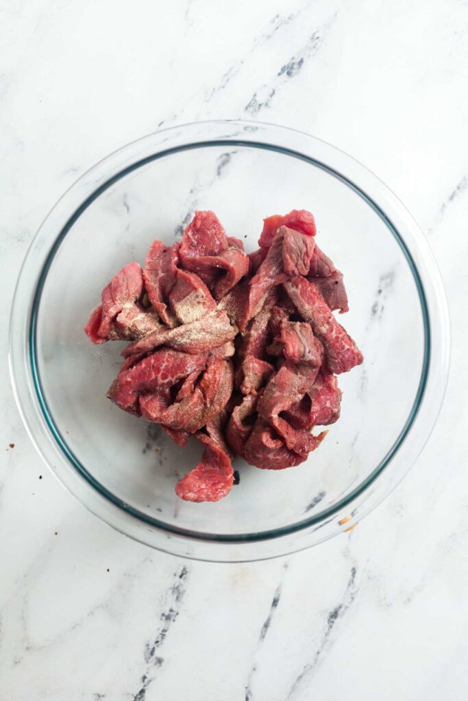 An overhead view of thinly sliced sirloin steak with seasonings added.