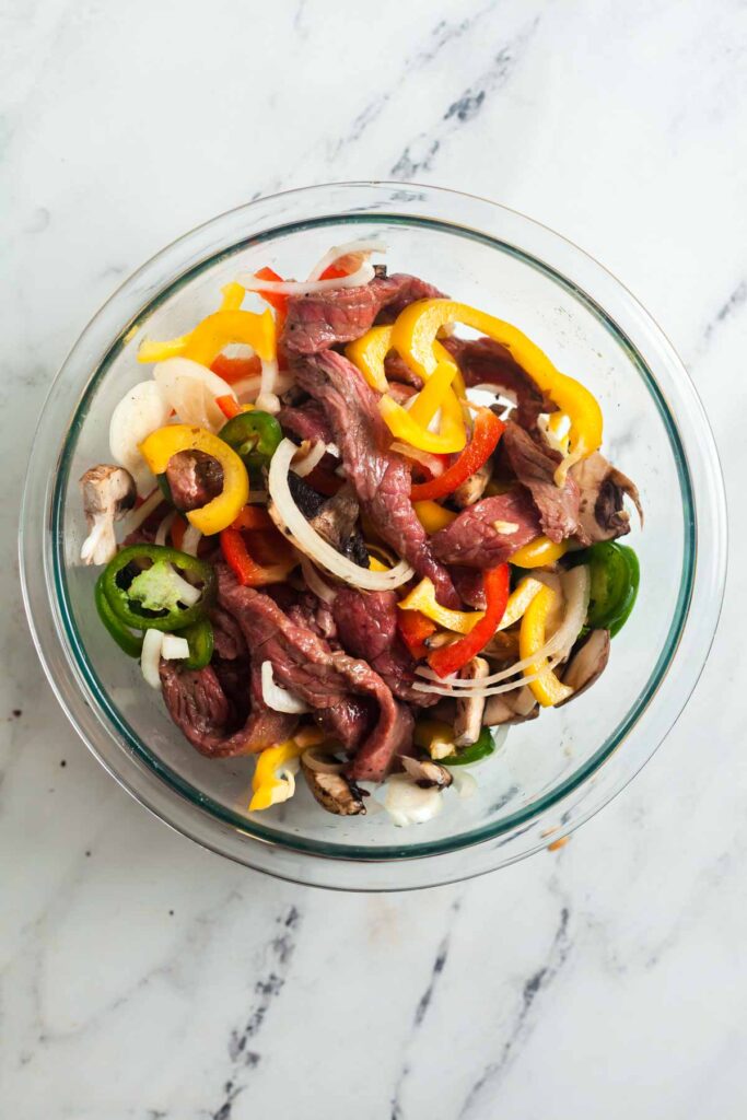 Mixing sliced vegetables into the marinaded steak to make easy Philly cheesesteak sandwiches.