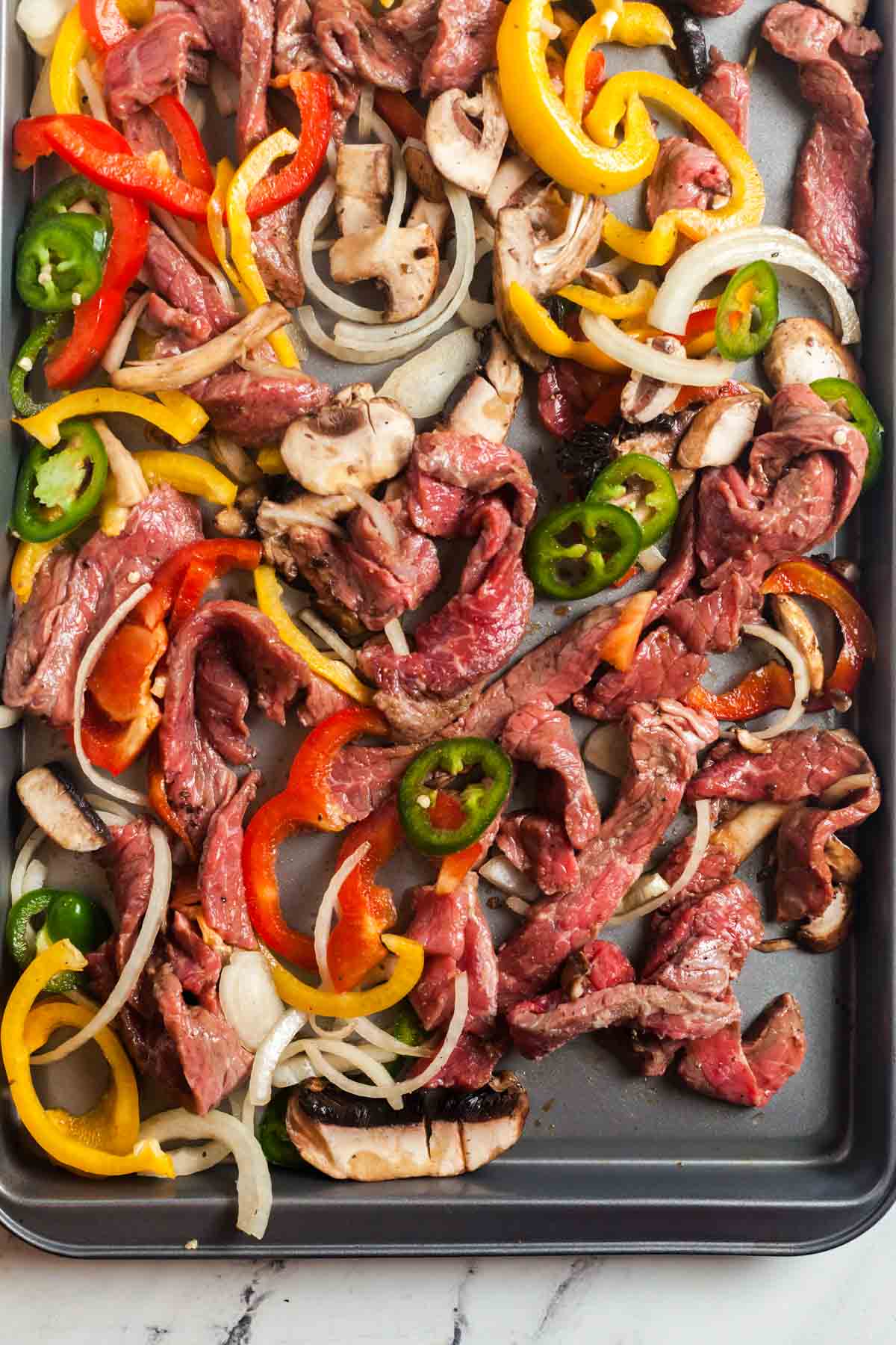 Image of the marinaded steak and vegetables on a sheet pan, ready to be baked.