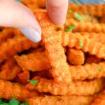Picking up a crinckle cut sweet potato fry from a platter of fries.
