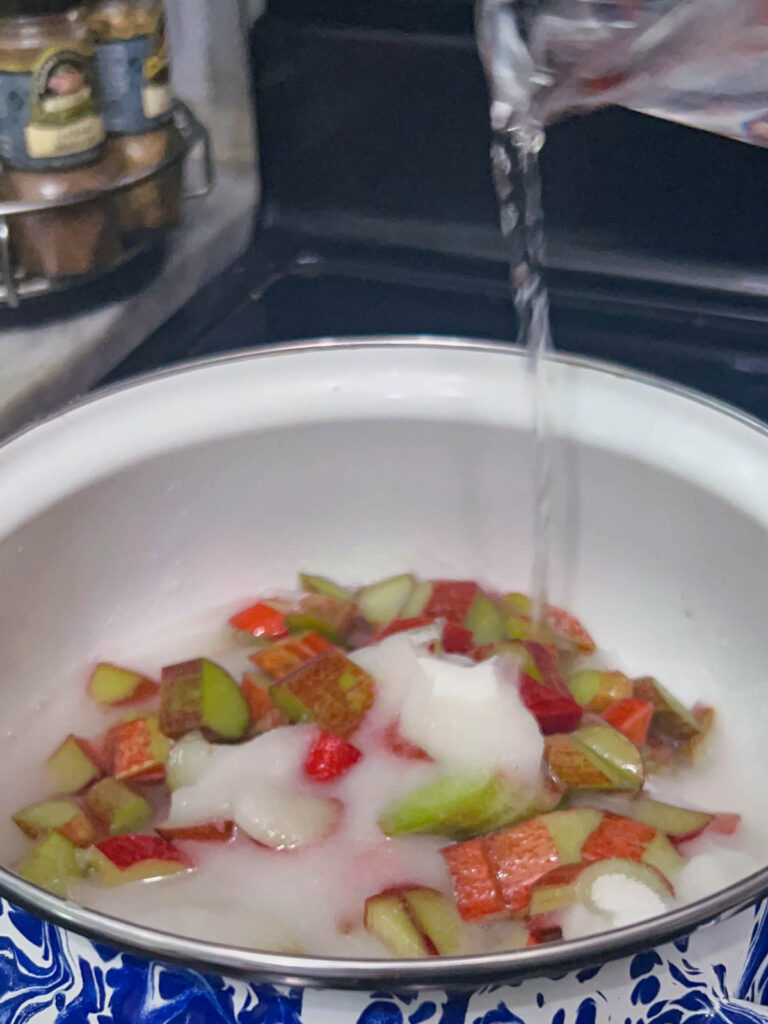 Adding sugar and water to a pot of rhubarb.