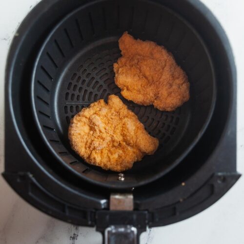 Frozen chicken in an air fryer basket.