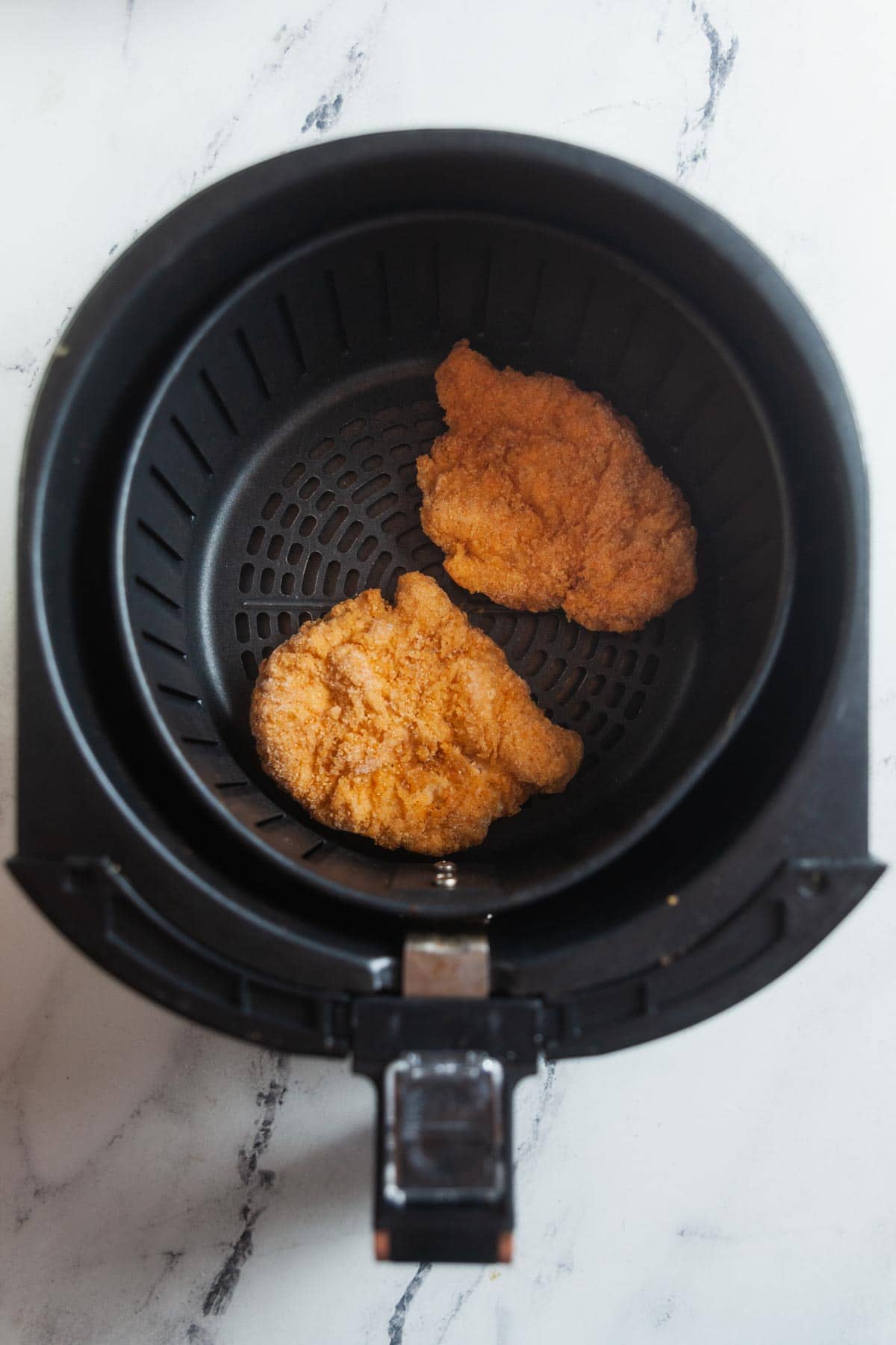 Frozen chicken in an air fryer basket.