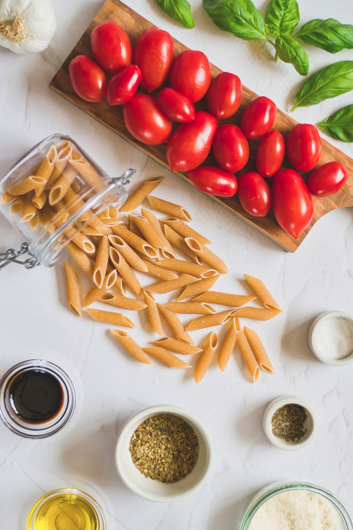 A flatlay showing the ingredients needed to make bruschetta pasta, including tomatoes, fresh basil, garlic, pasta, and spices. 