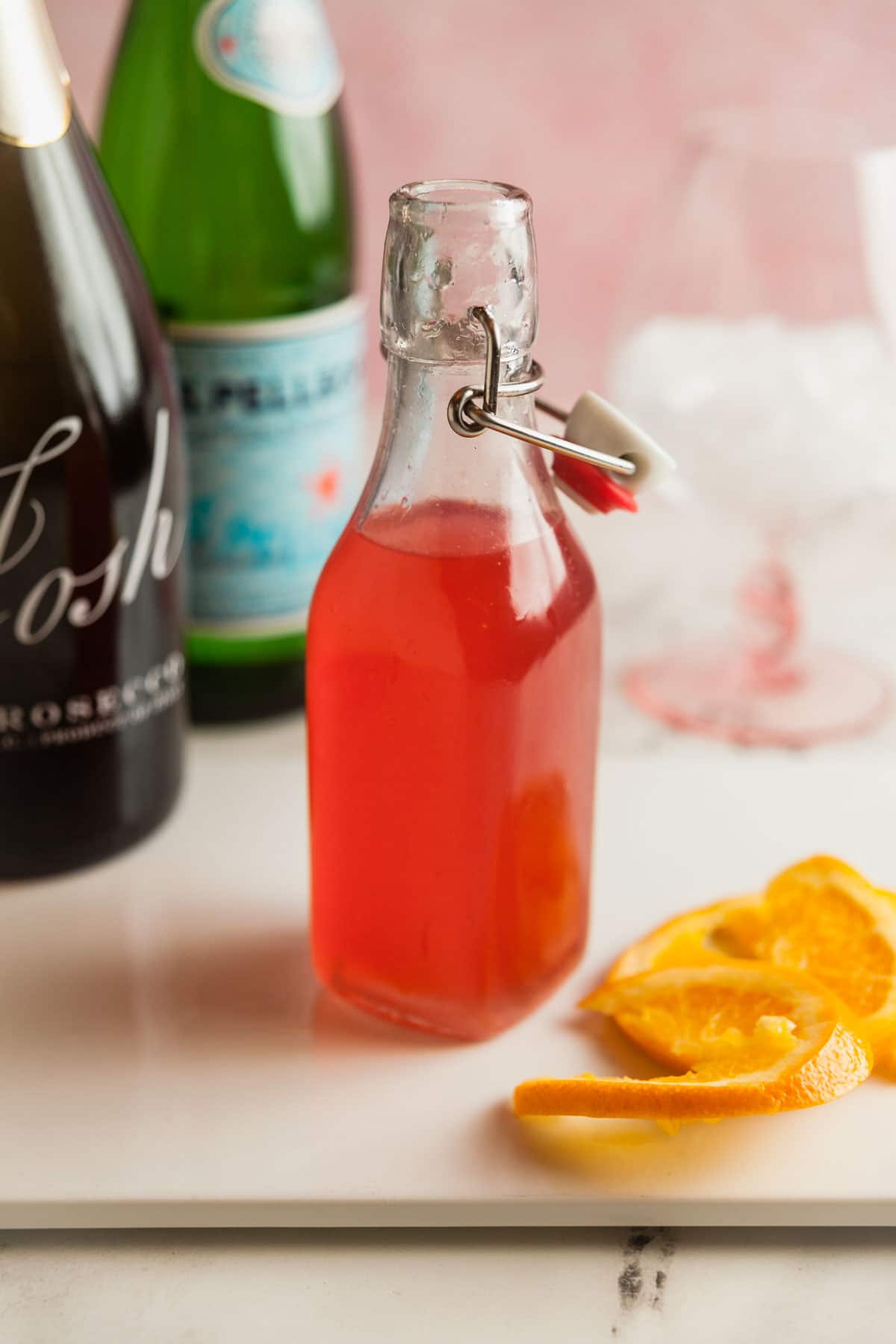 Ingredients needed to make a rhubarb spritz, including homemade rhubarb syrup, prosecco, and sparkling water.