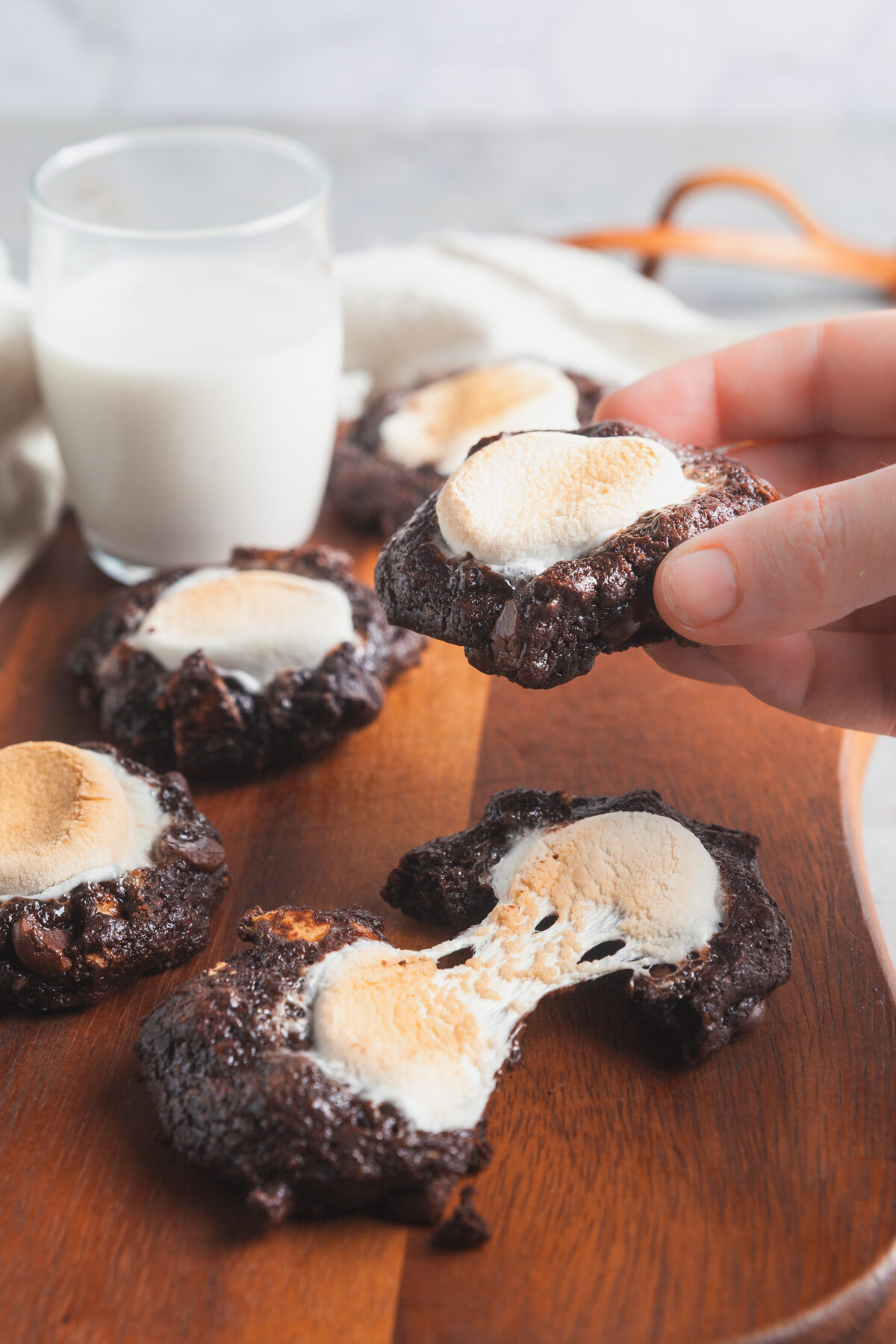 Picking up a chocolate marshmallow cookie from a platter of cookies, with a glass of milk in the background. 