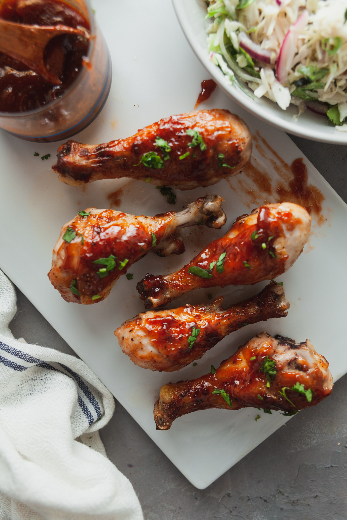 BBQ chicken Thights on a white serving board, with a bowl of coleslaw to the side.
