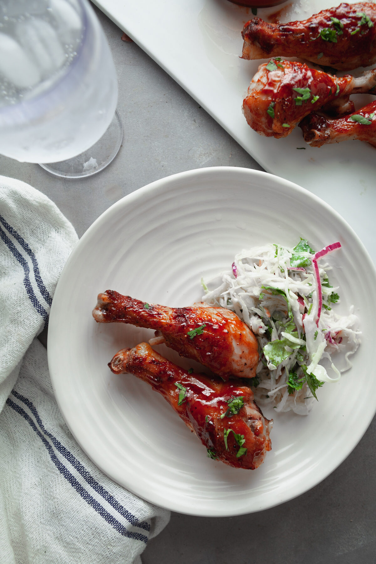A white plate with two chicken legs and a side of coleslaw. 