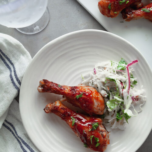 A white plate with two chicken legs and a side of coleslaw.