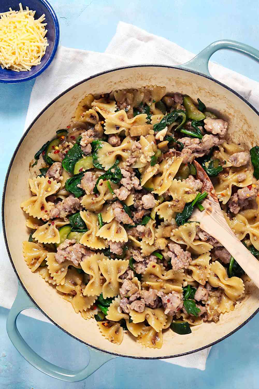 An overhead view of bowtie pasta with crumbled sausage and vegetables in a shallow blue pan.