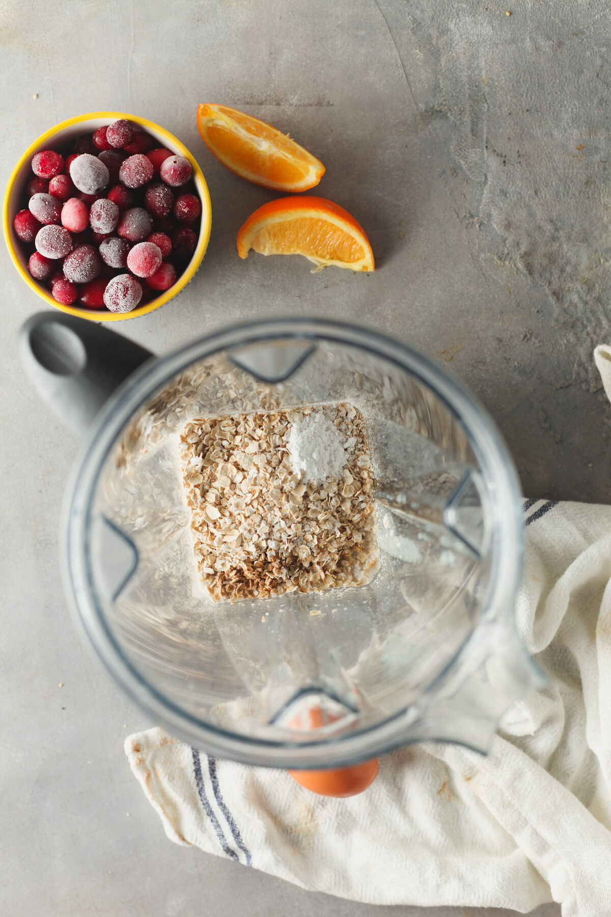 Dry ingredients for baked oats in a blender, with cranberries and an orange off to the side. 