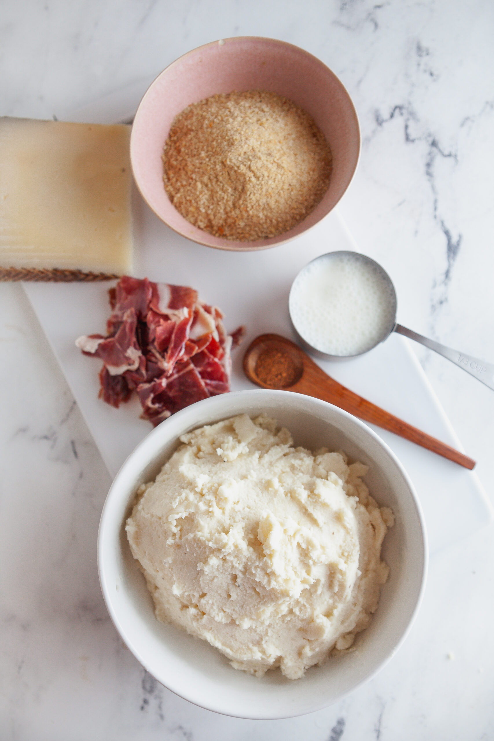 Ingredients needed to make ham and potato croquettes on a white marble board.