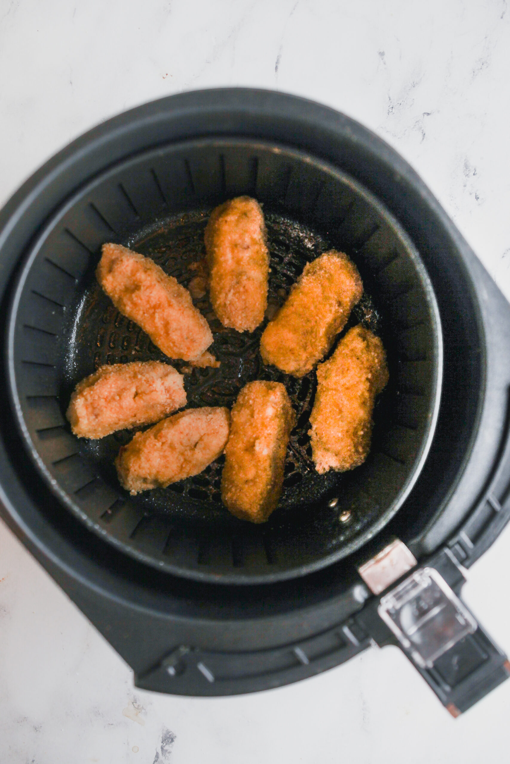 An air fryer basket filled with air fried potato croquettes.