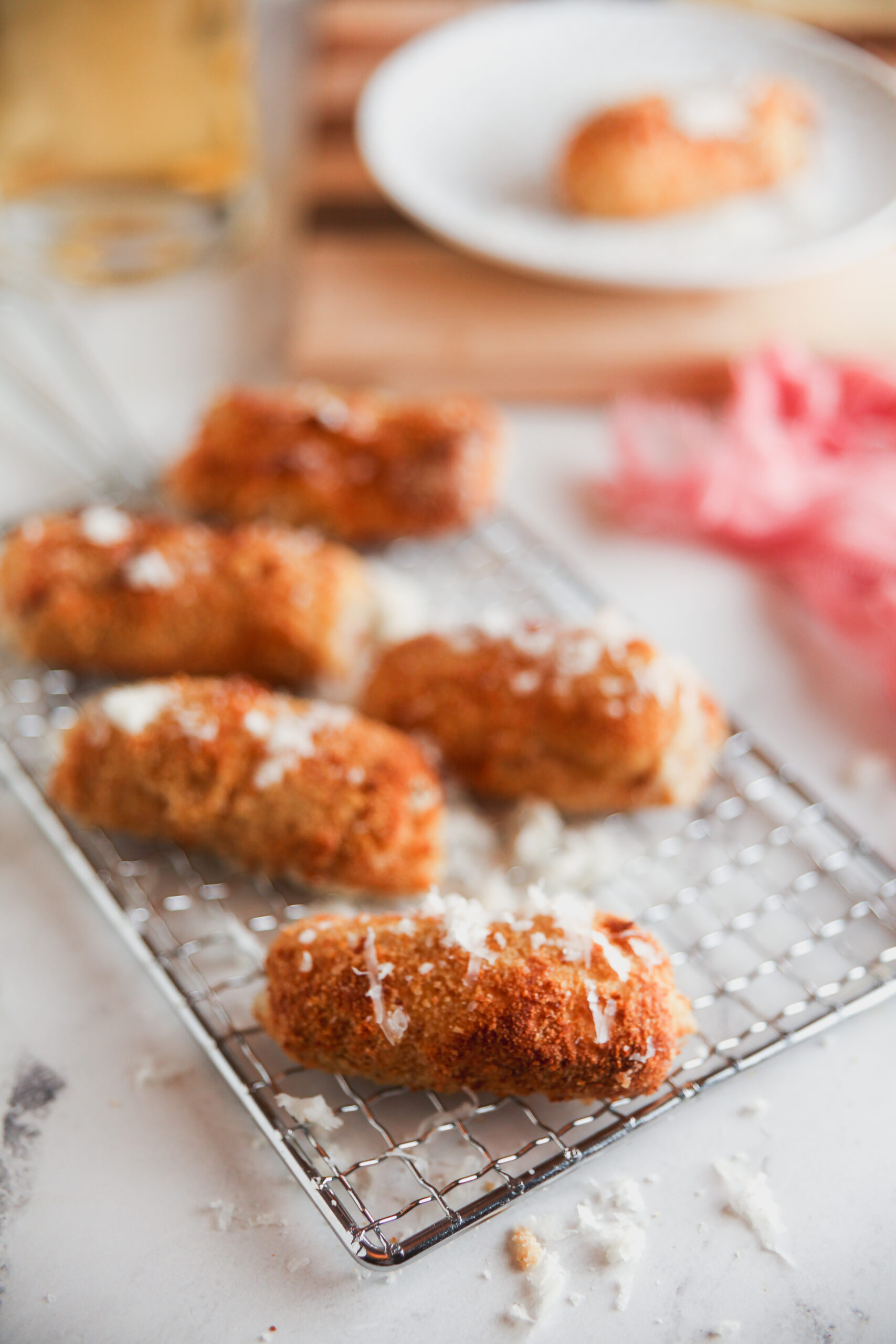 Air fryer croquettes topped with cheese on a cooling rack.