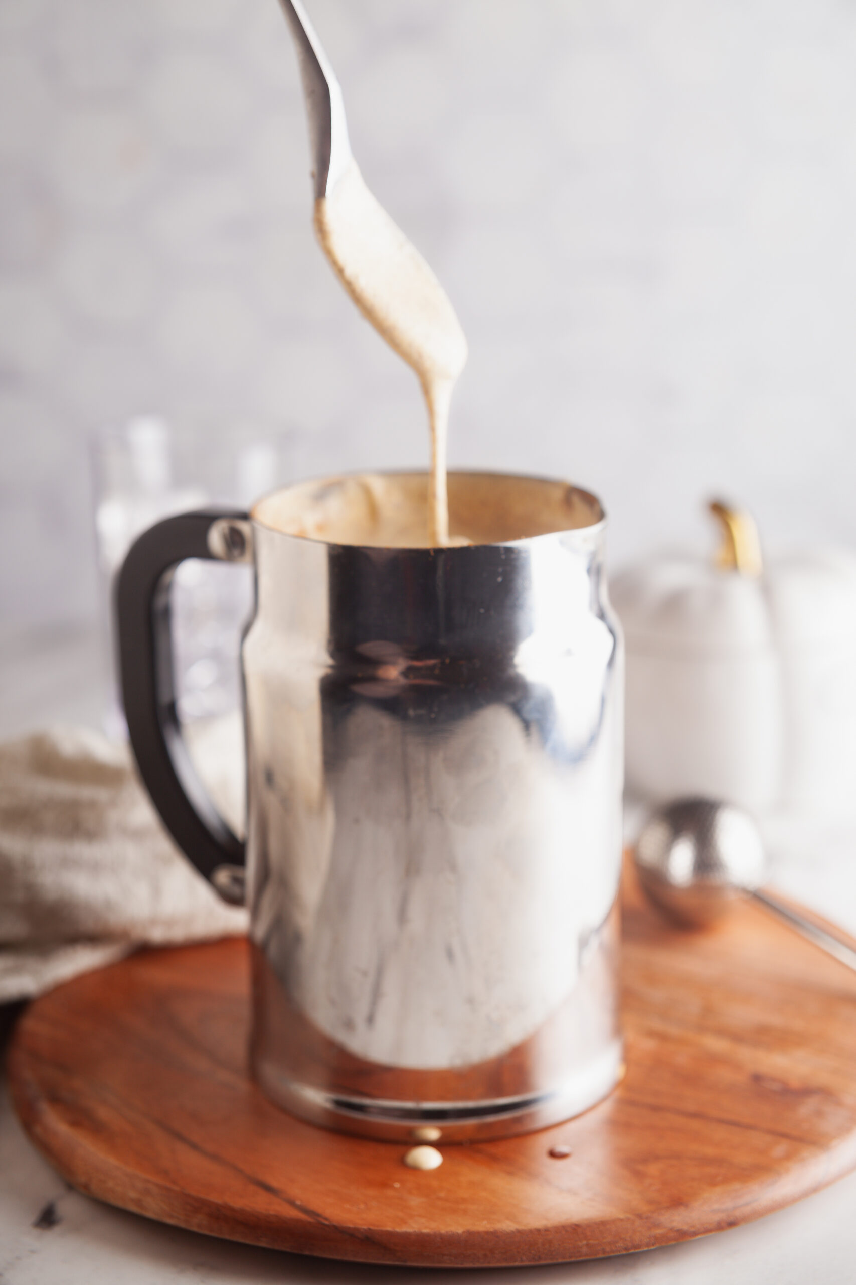 A spoon of pumpkin cream cold brew dripping into a milk frother. 