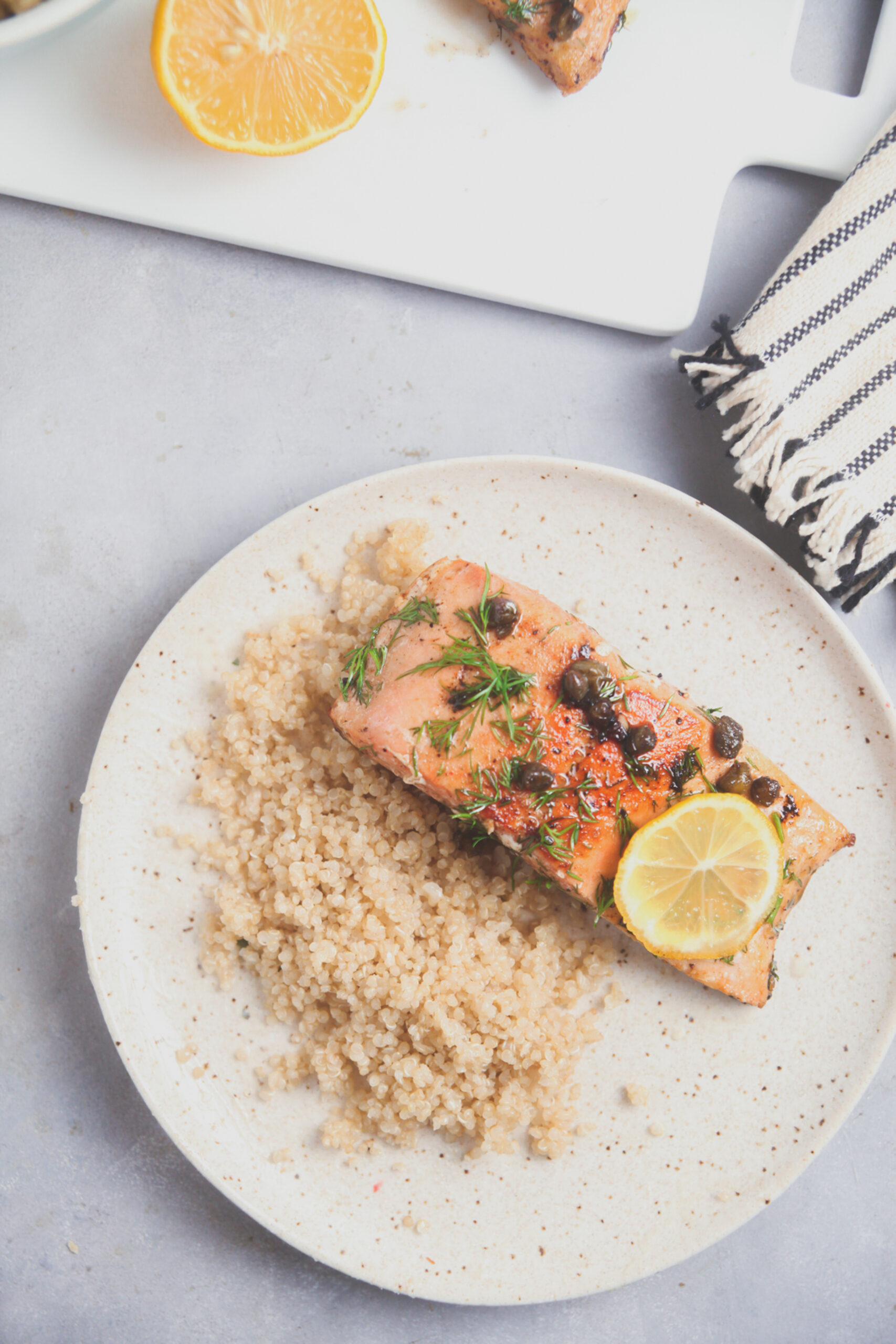 Overhead image of salmon with lemon caper sauce plated with quinoa and lemons on a white plate.