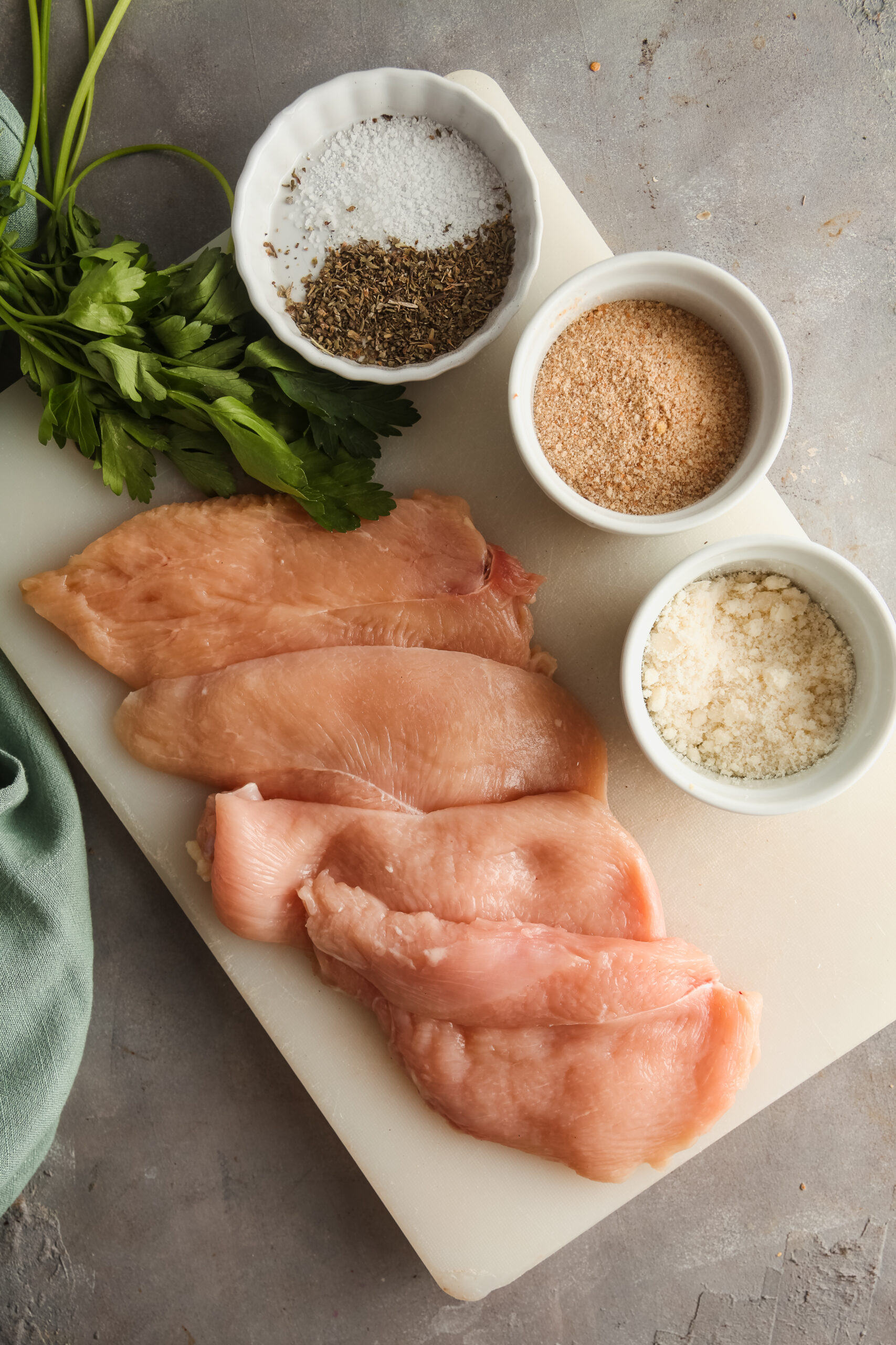 Overhead view of ingredients needed to make breaded chicken cutlets in the air fryer, including chicken breast filets, breadcrumbs, cheese, and seasonings.