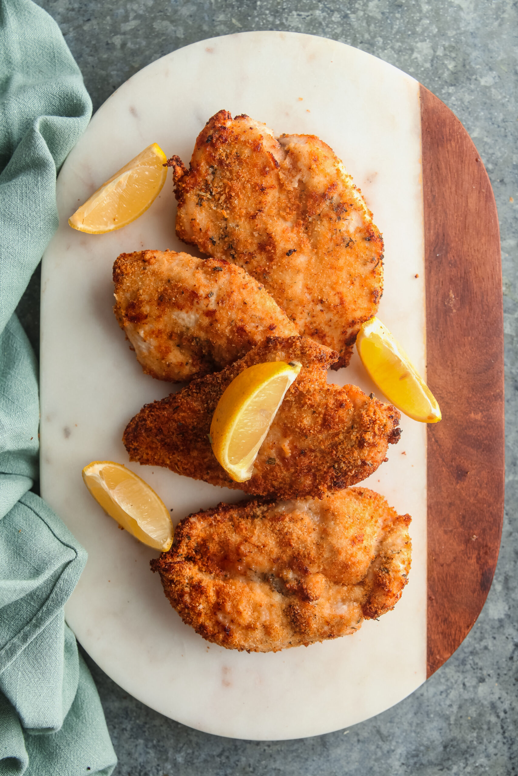 An overhead view of a platter of air fried chicken cutlets topped with lemon wedges.