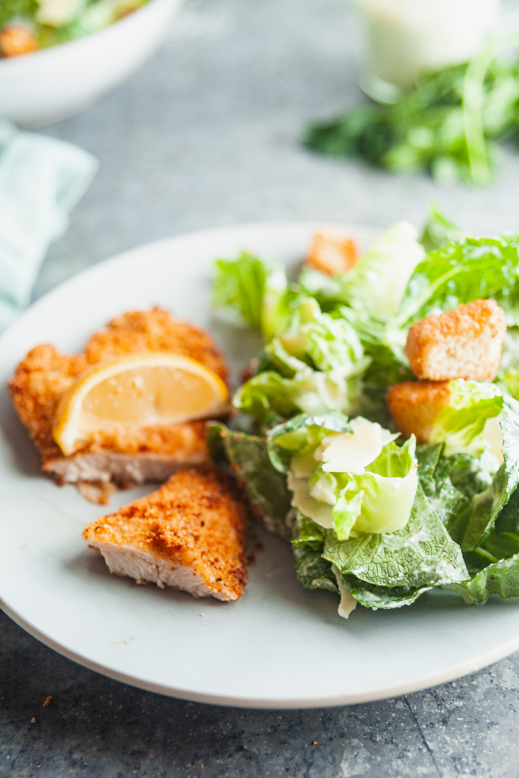 A light blue plate with a sliced chicken cutlet made in the air fryer and a caesar salad.