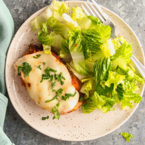 Air fryer chicken parmesan with salad on a speckled plate.