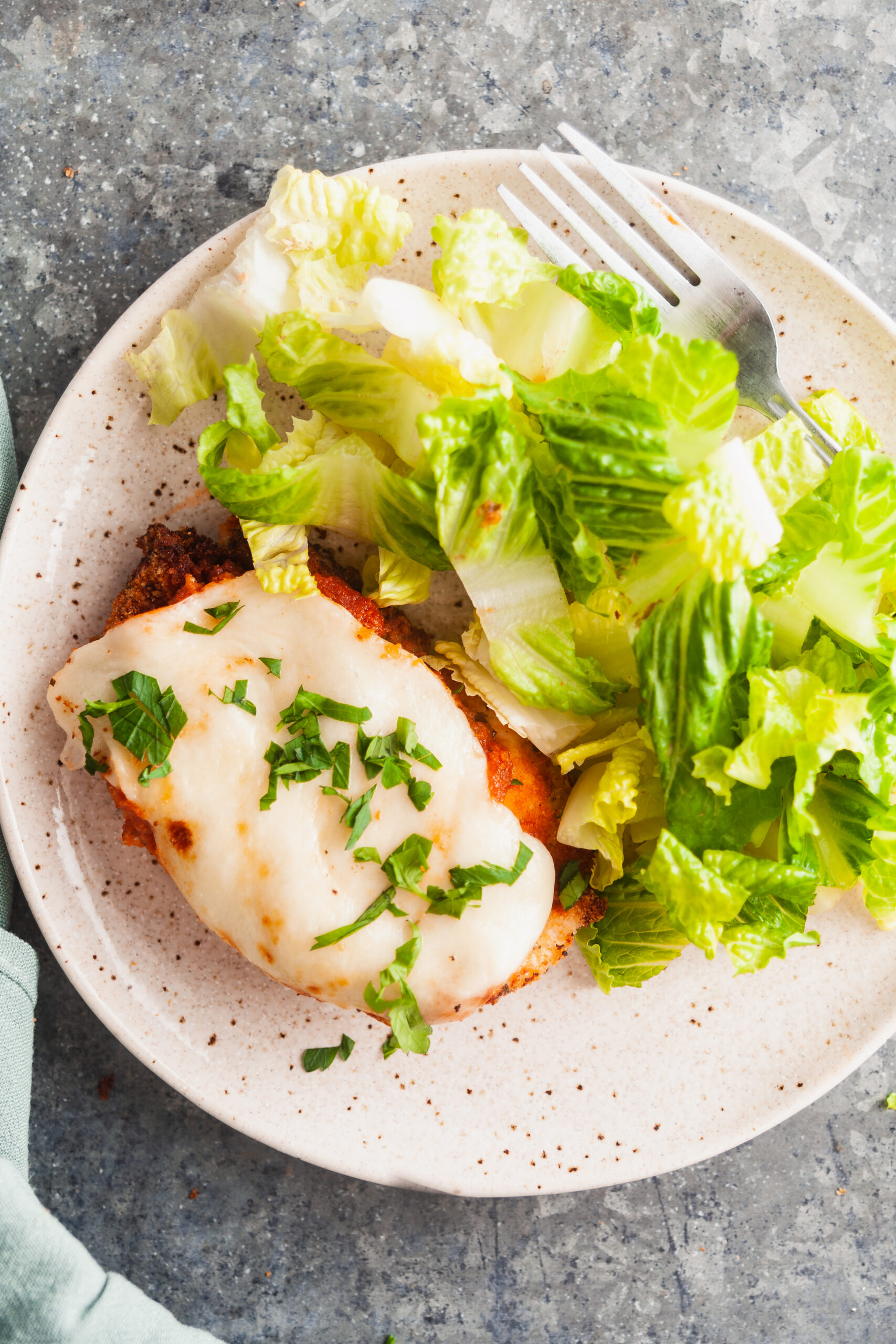 Overhead view of chicken parm plated with a green salad.