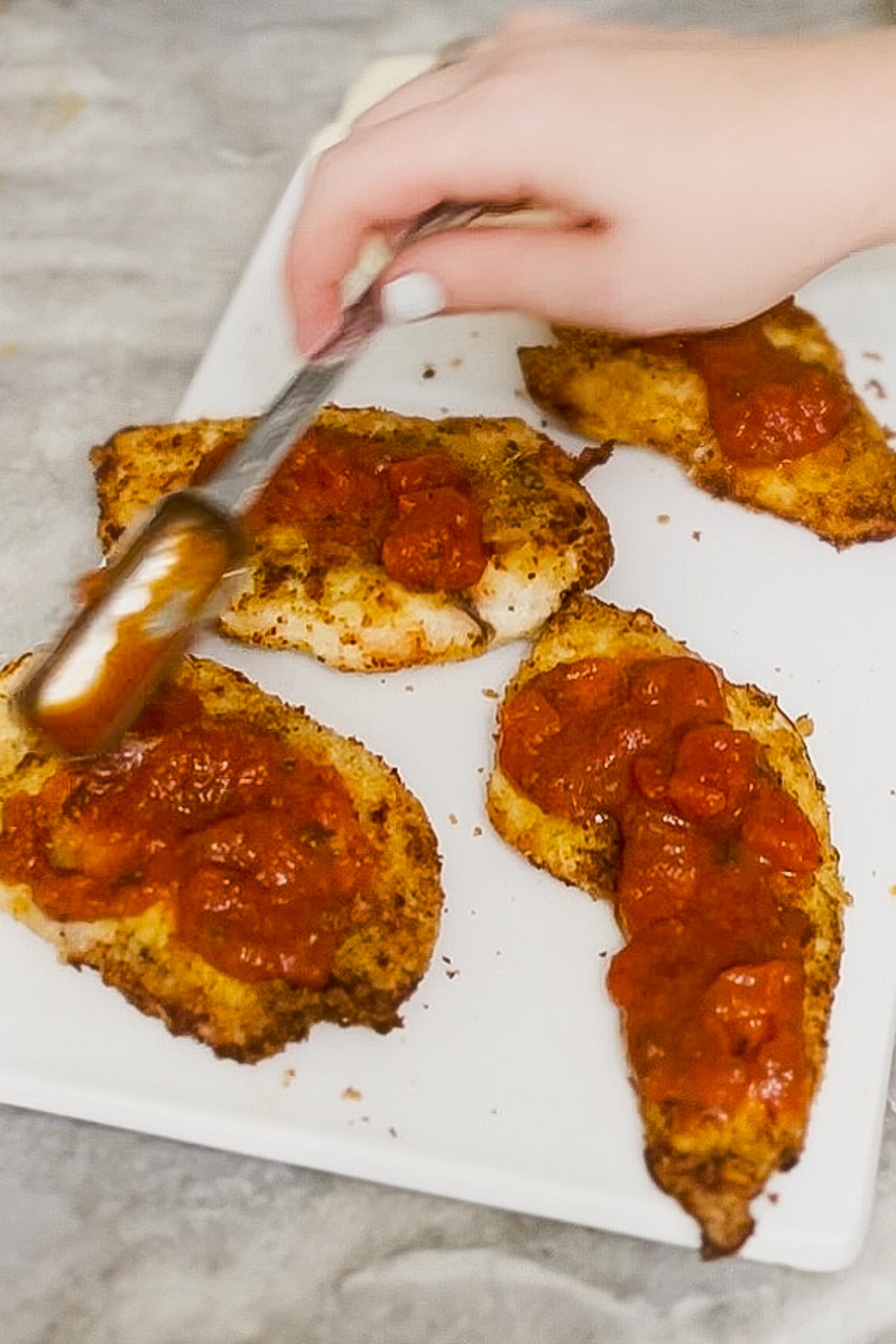 Spreading sauce onto chicken cutlets.