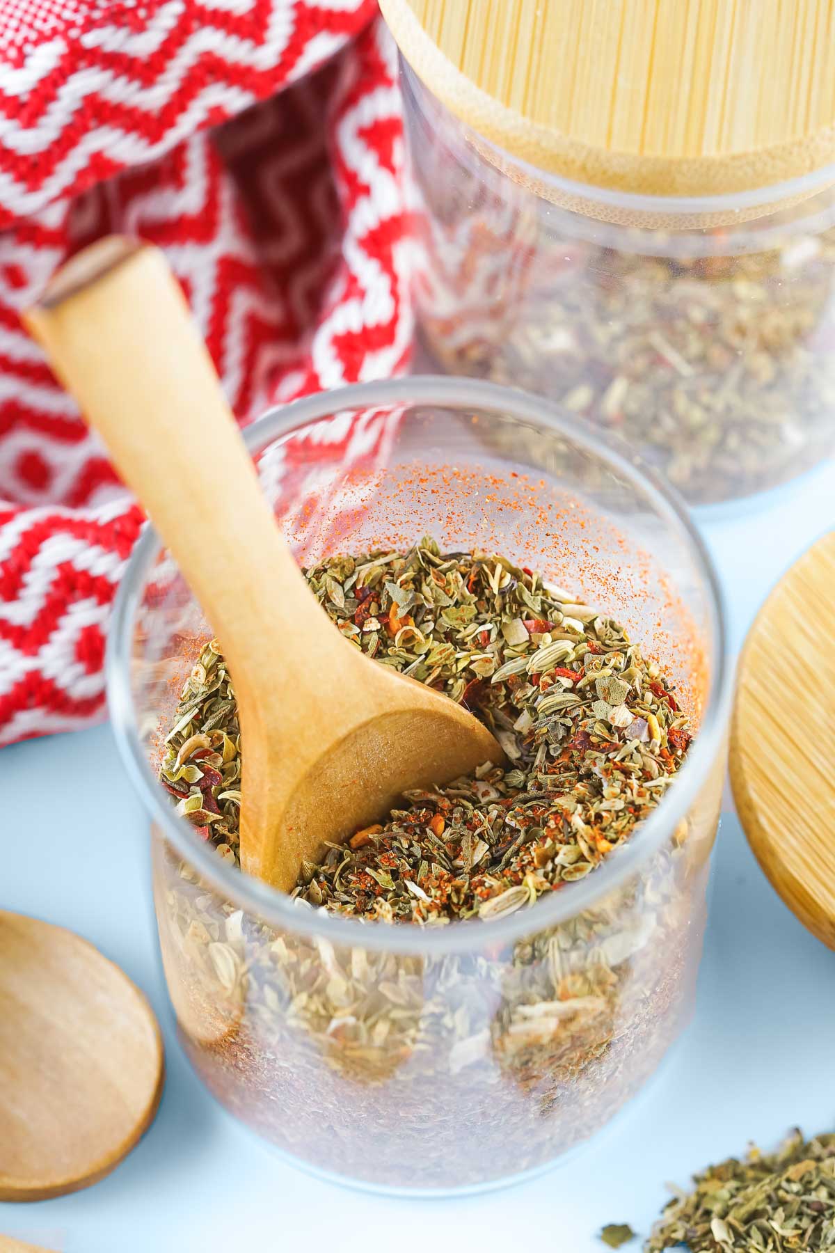 A small jar of homemade pizza seasoning with a wooden scoop in it. 