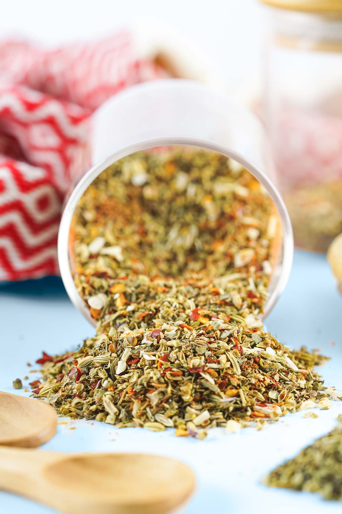 A tipped over container of pizza seasoning, with some spilling out onto a light blue background. 
