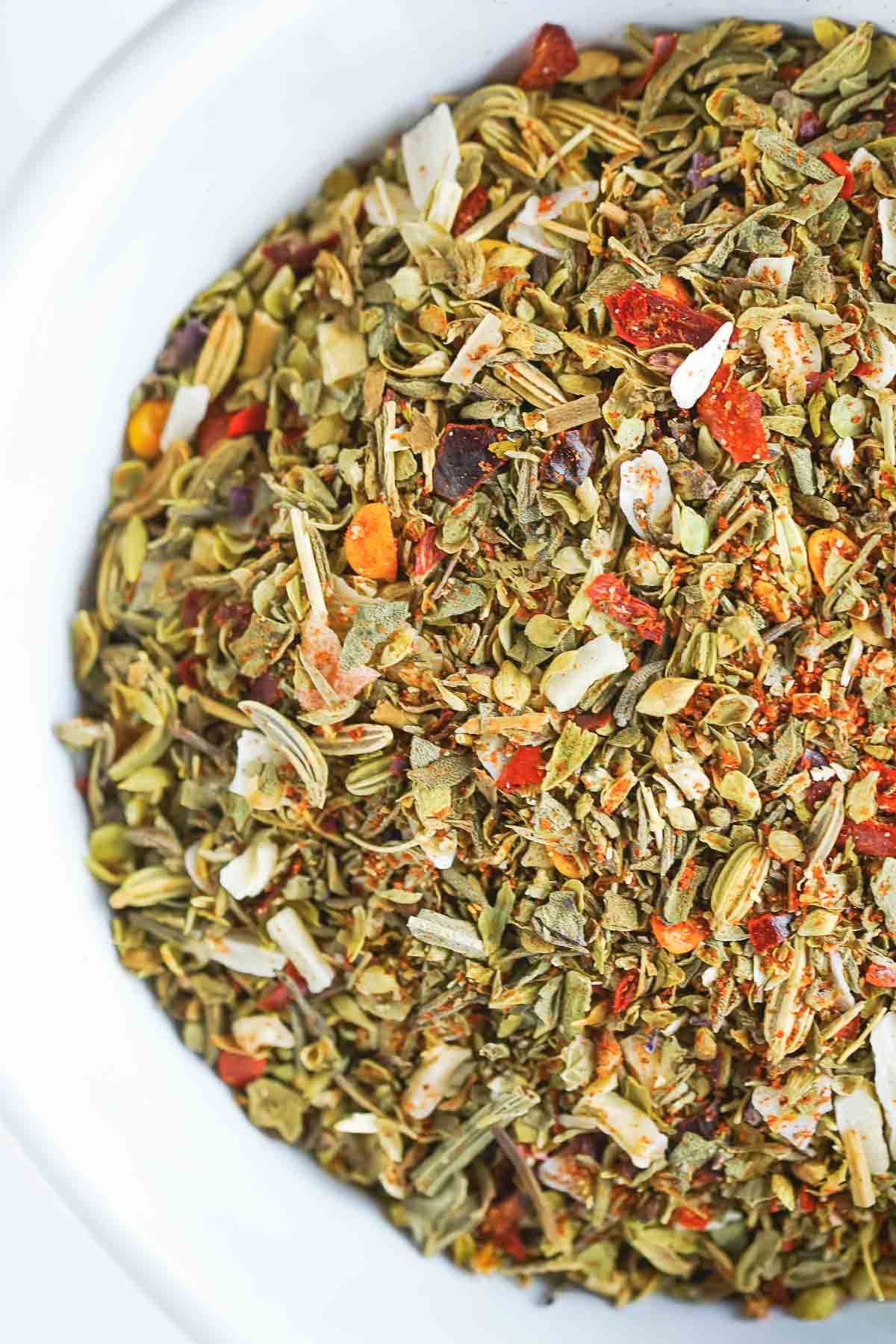 Closeup view of homemade pizza seasoning blend in a white bowl. 
