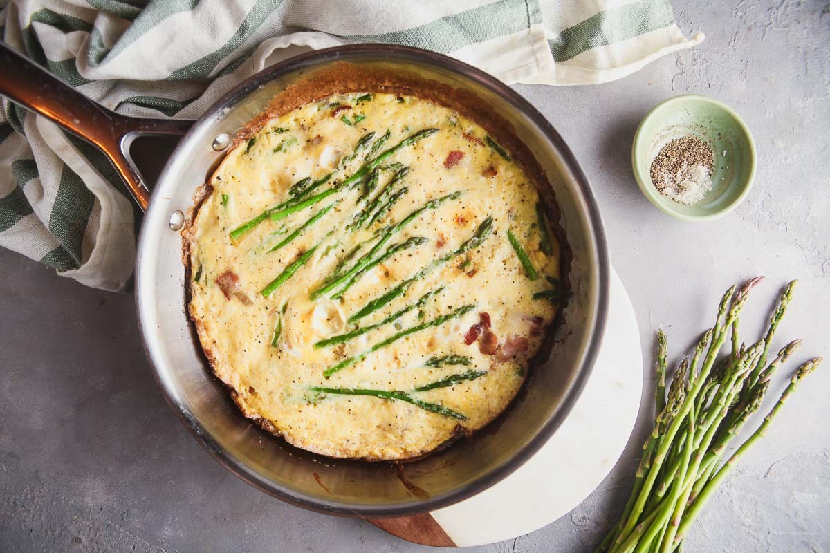 Overhead view of an asparagus frittata in a stainless skillet. 