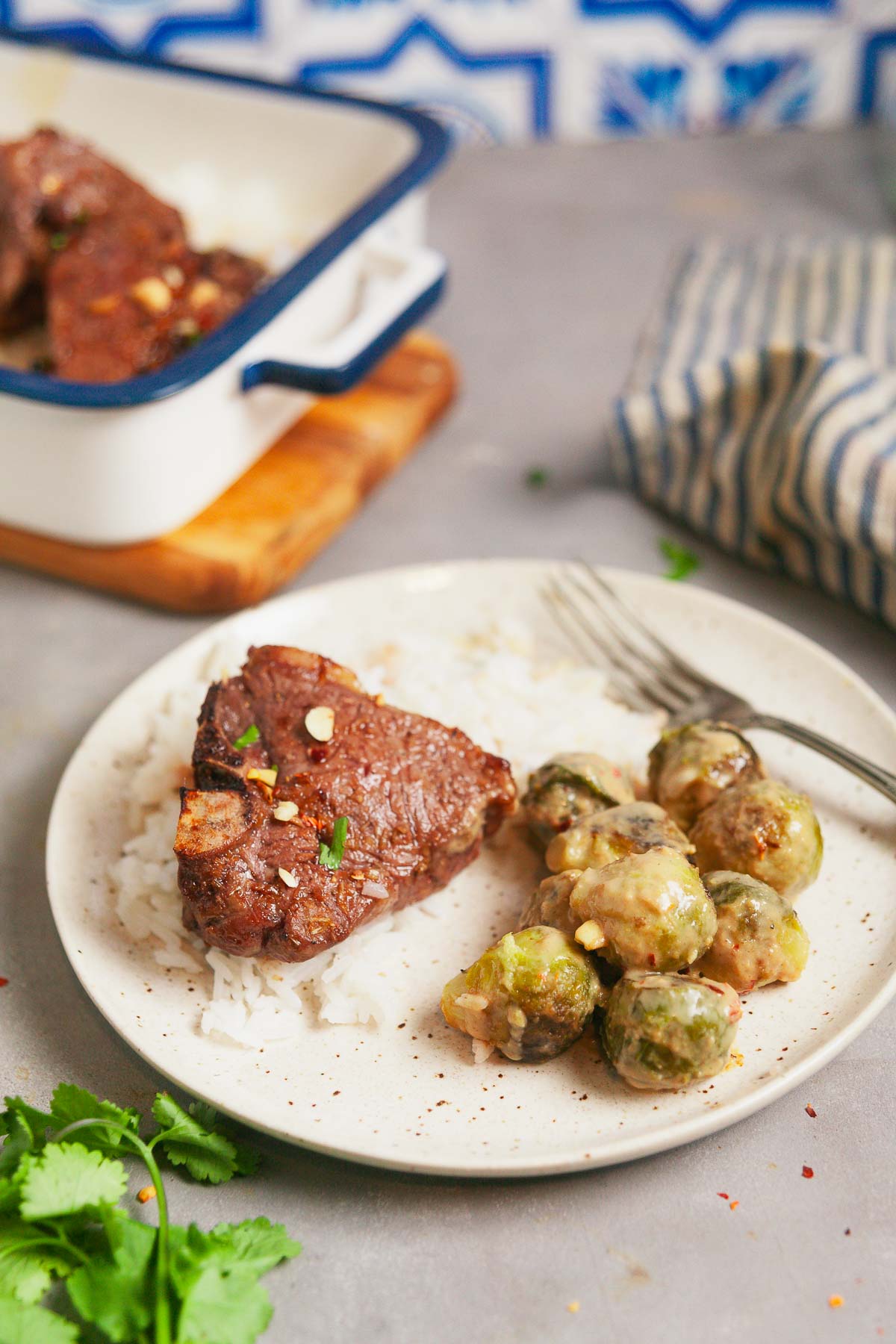 Plated lamb chop over rice with a side of peanut Brussels sprouts.