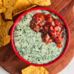 Overhead view of white spinach queso in a red serving dish.