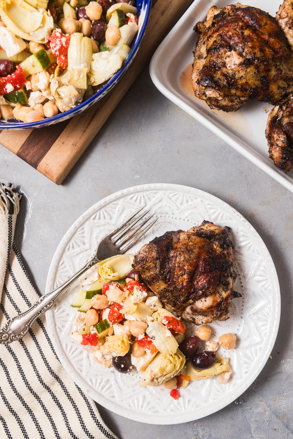 Artichoke and chickpea salad plated with a grilled chicken thigh. 