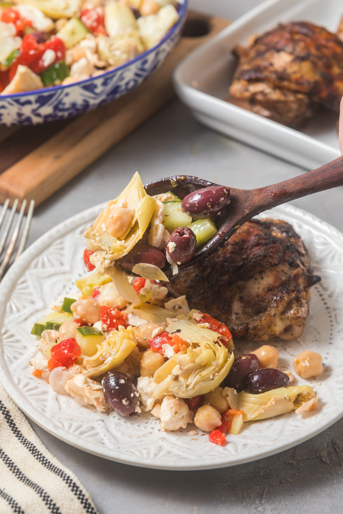 Spooning the chickpea salad onto a plate with grilled chicken. 