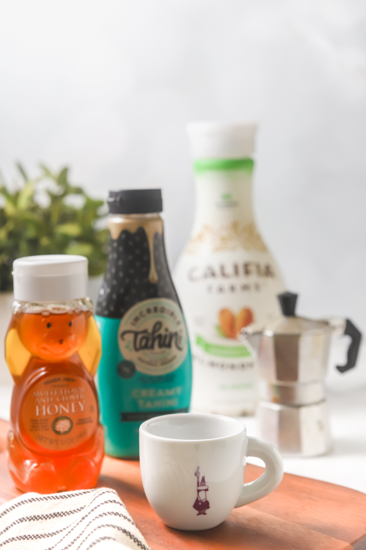Ingredients to make a halva latter, including tahini, honey, espresso, and almond milk, arranged on a marble counter.