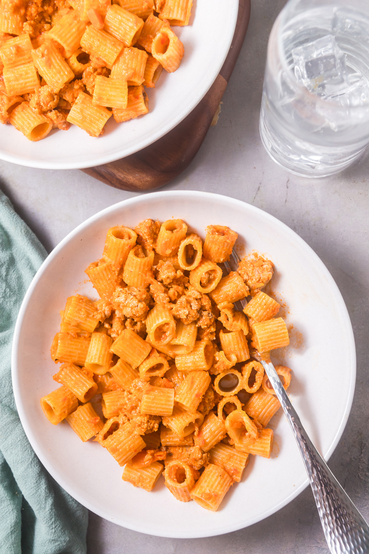 An overhead view of two plates of rigatoni pasta tossed in a ground pork and red curry sauce inspired by bolognese. 