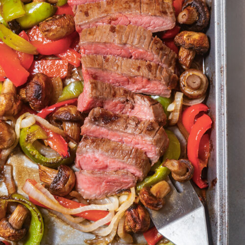 Overhead view of a sheet pan steak dinner with mushrooms, onions, and potatoes, on the pan.
